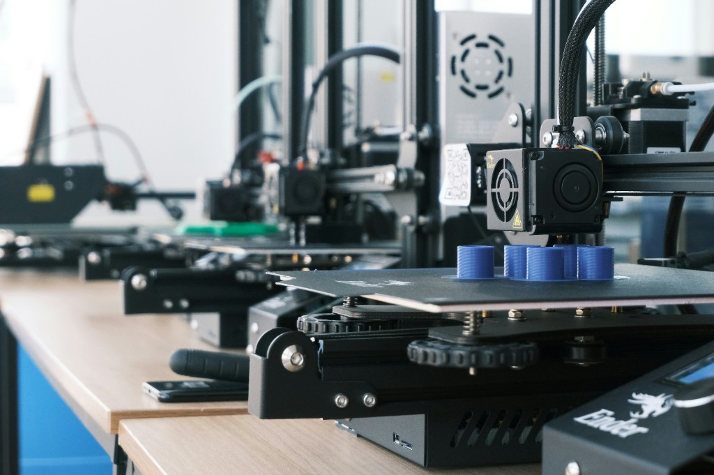 A row of 3D printers in a workshop, focusing on blue parts being printed